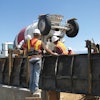 A four-man crew works quickly to pour and finish a typical parapet. One worker uses a power vibrator to consolidate the concrete for uniform density and blend the concrete together into a single solid mass.