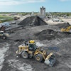 Teleo-equipped Caterpillar wheel loader operating in the midst of other operations across an Ajax Paving asphalt plant.