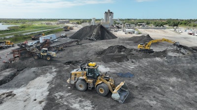 Teleo-equipped Caterpillar wheel loader operating in the midst of other operations across an Ajax Paving asphalt plant.
