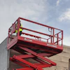Red scissor lift raised next to warehouse building and shipping container