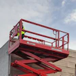 Red scissor lift raised next to warehouse building and shipping container