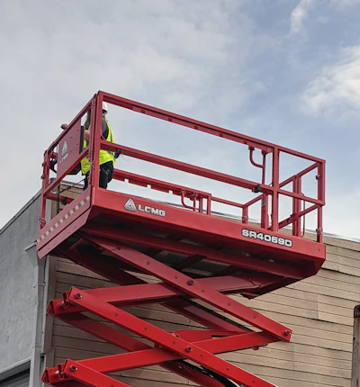 Red scissor lift raised next to warehouse building and shipping container