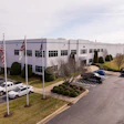 Corporate office building with flags, landscaped parking area and parked vehicles