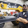 An RDO service technician takes a break from an inspection in front of a John Deere Motor Grader.
