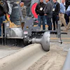 Industrial soil compactor machine displayed at outdoor trade show with attendees in hard hats observing the equipment