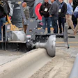 Industrial soil compactor machine displayed at outdoor trade show with attendees in hard hats observing the equipment