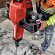 Construction worker using red Hilti pneumatic breaker on concrete surface