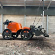 Orange and black agricultural tractor with attached hydraulic implement in industrial yard