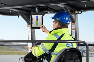 Construction worker in safety gear operating thermal imaging equipment on Volvo machinery outdoors