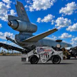 Decommissioned aircraft tail suspended above white ground support tug vehicle in desert aviation facility