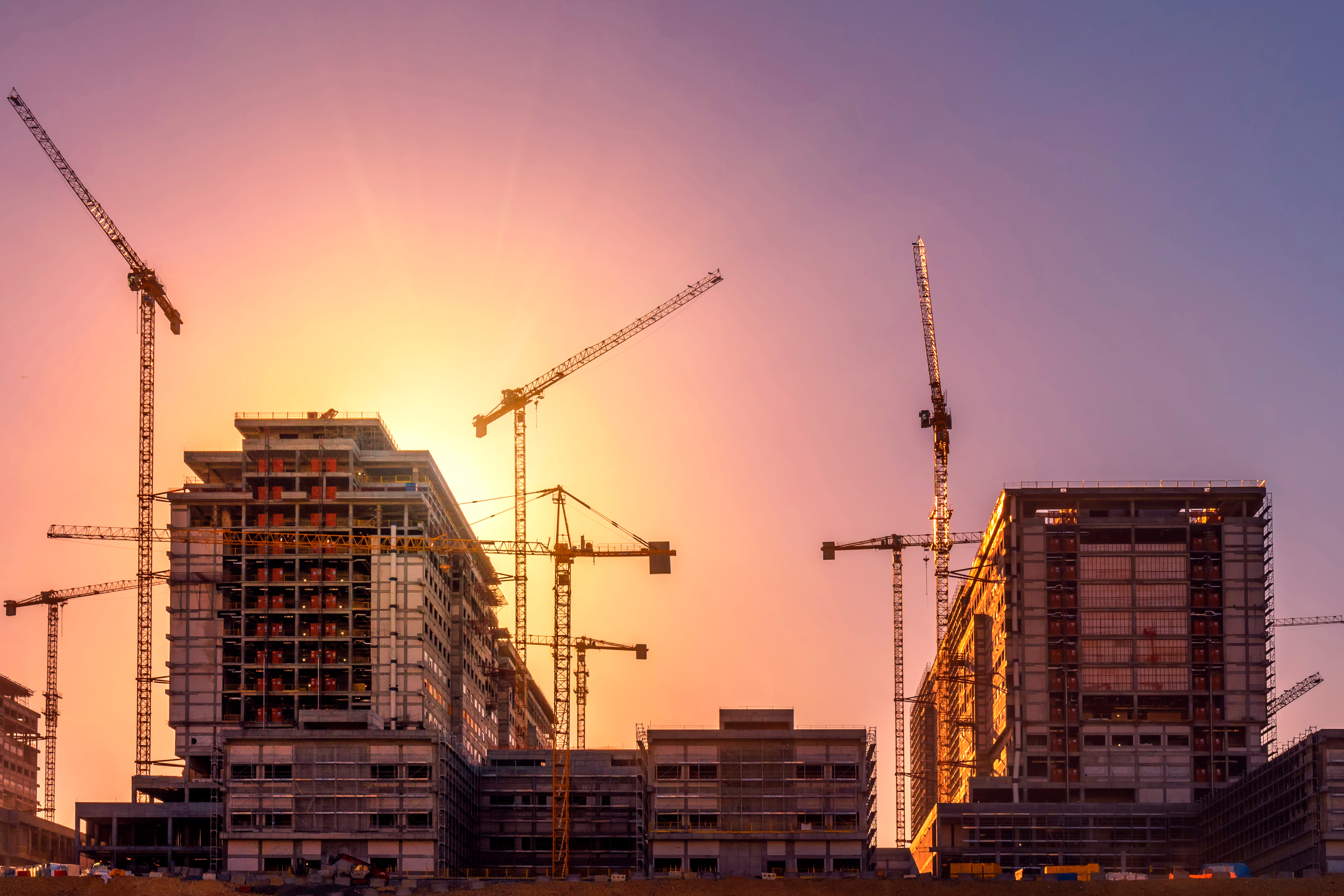 Construction site at sunset with multiple cranes and high-rise buildings under development