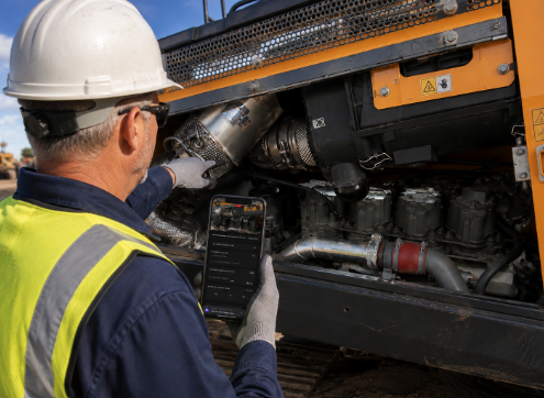 Construction worker in safety gear inspecting engine components of orange industrial truck