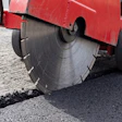 Red asphalt cutting machine with circular saw blade cutting through road pavement
