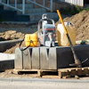 Construction site with compactor, safety vest, fuel container, and tools on concrete foundation
