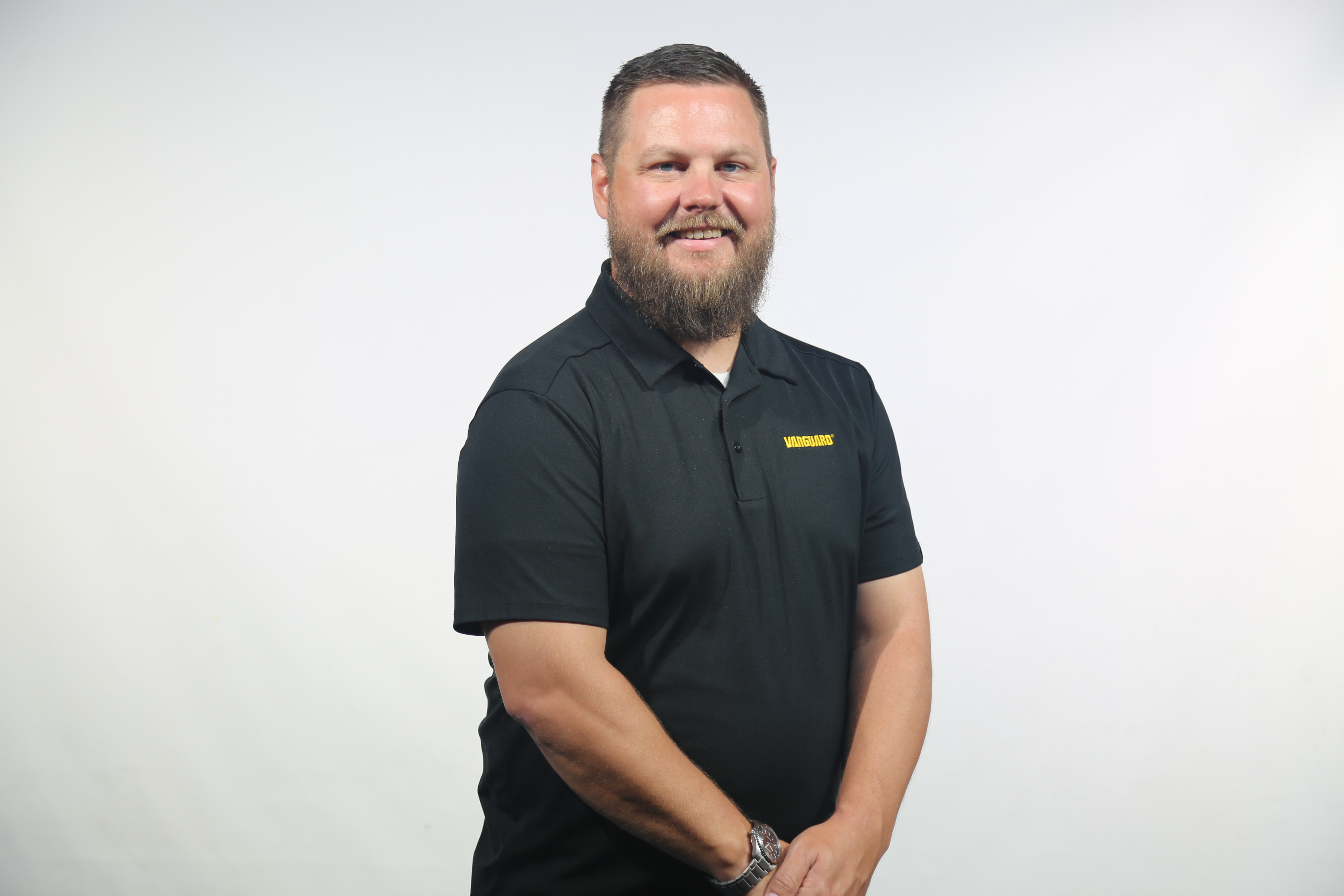 Professional man with beard wearing black DeWALT polo shirt, smiling at camera against white background Headshot