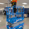 Worker in safety gear operating blue Genie GS-1932m scissor lift indoors