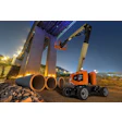 Orange JLG telescopic boom lift operating at dusk near large industrial pipes and concrete structure