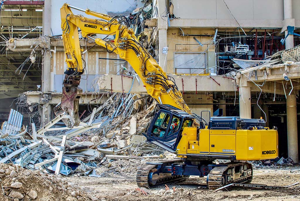 Yellow Kobelco excavator demolishing concrete building structure at construction site