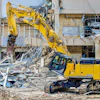 Yellow Kobelco excavator demolishing concrete building structure at construction site