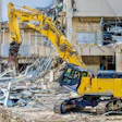 Yellow Kobelco excavator demolishing concrete building structure at construction site