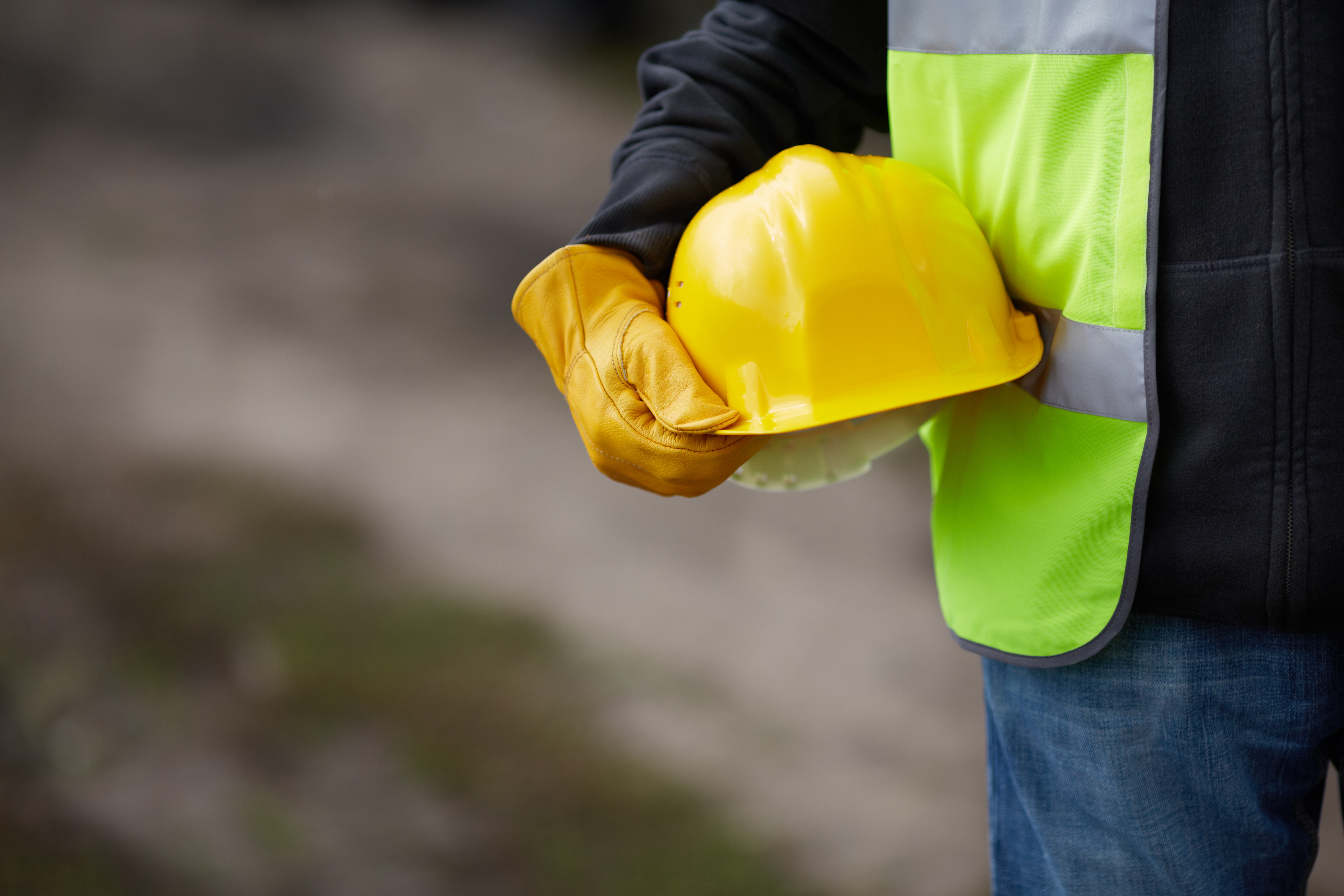 Construction worker holding yellow hard hat wearing neon safety vest and brown gloves