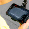 Worker in yellow safety vest holding rugged tablet displaying surveying or mapping software outdoors