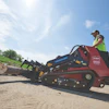 Worker operating a Toro wood chipper on a construction site with logs and materials nearby
