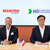 Two business executives at a formal meeting with Manitou Group and HD Construction Equipment logos, French and South Korean flags on table