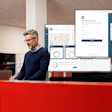 Professional man at red desk reviewing analytics dashboards and software interfaces on multiple computer monitors