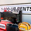Worker using payment terminal on rental equipment truck with 1-800-UR-RENTS phone number and tools visible