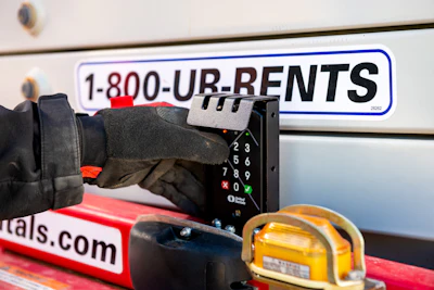 Worker using payment terminal on rental equipment truck with 1-800-UR-RENTS phone number and tools visible