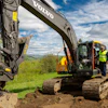 Volvo excavator operating on construction site with worker in safety gear