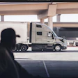 Silhouetted person viewing white commercial truck parked beneath highway overpass in industrial setting