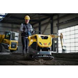 Construction worker operating yellow Wacker Neuson compactor in industrial warehouse setting