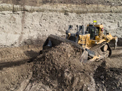 Yellow bulldozer pushing soil and earth in an active quarry excavation site with exposed rock face