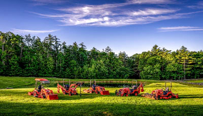 Red farm tractors and equipment lined up in a green field with forest trees under blue sky