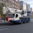 White and blue Tadano mobile crane truck parked on urban street with city buildings in background