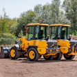 Yellow Volvo wheel loader and vibratory rollers parked on construction site with trees in background
